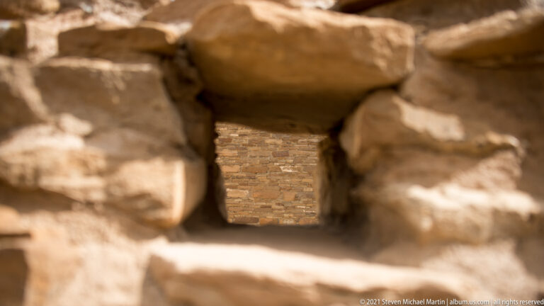 A heavy stone lintel spans a narrow opening in a wall of stacked masonry blocks.
