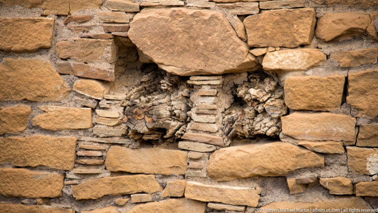 Large sandstone blocks and thin chinking stones form a close-up view of a weathered masonry wall.