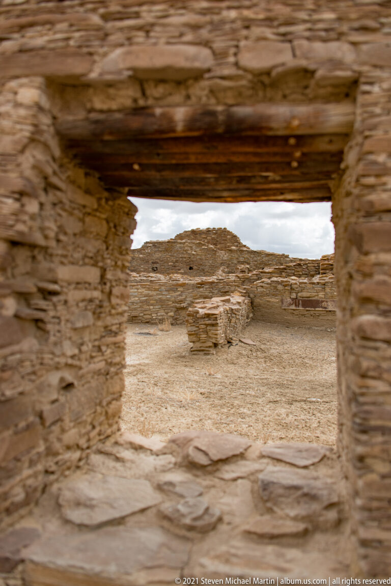 A courtyard and low stone structure appear through a thick, softly blurred masonry doorway.