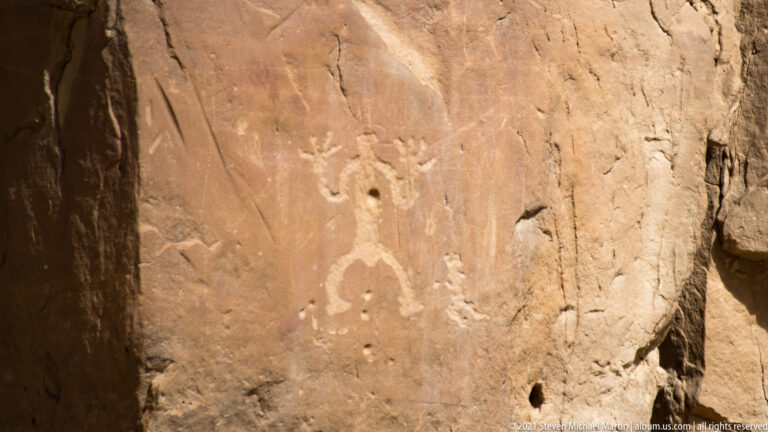 A sandstone panel bears a prominent spiral and several smaller pecked symbols, including a human-like figure.