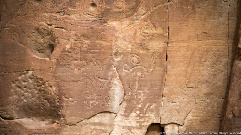 Pecked circles, simple human-like figures, and geometric marks cover a cracked sandstone panel.