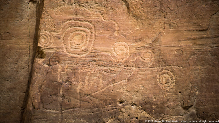 Nested circles and ring-shaped petroglyphs are carved across a horizontal sandstone surface.