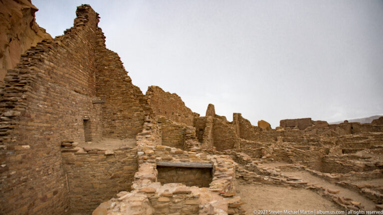 A narrow doorway through thick stone walls frames another opening and a room beyond.