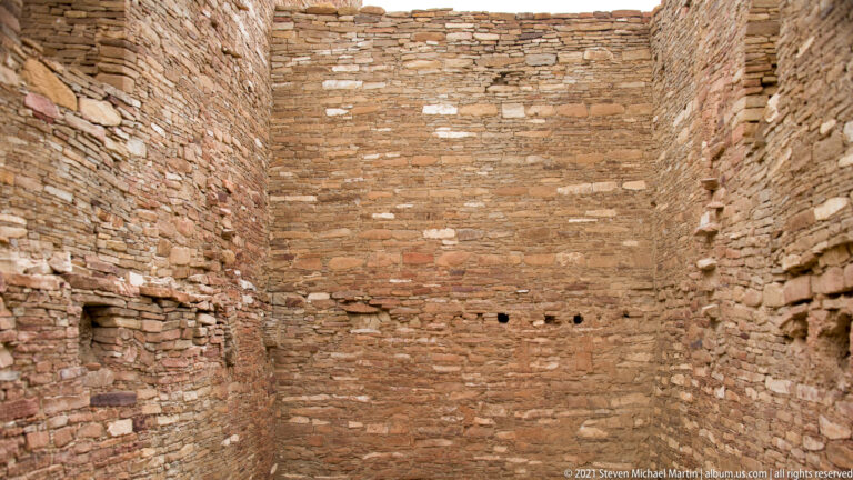 Tall stone walls enclose a rectangular room with several small openings near the floor and a low recess at left.