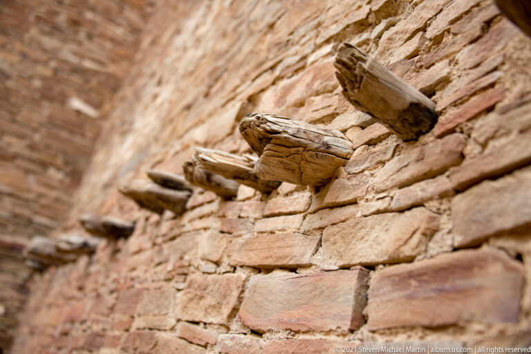 Short weathered wooden beams protrude from a sloping stone wall in a close architectural detail.
