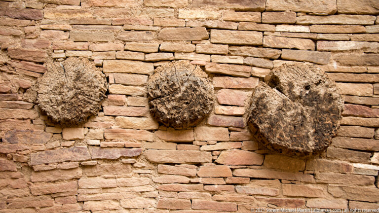 Three rough rounded forms project from a wall of thin stacked sandstone courses.