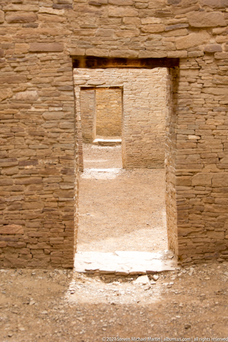 Two aligned stone doorways lead from a shaded room into a brighter interior beyond.
