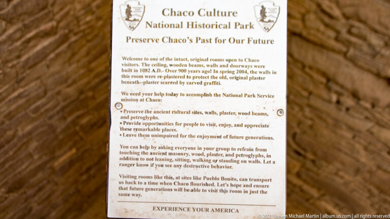 A preservation sign for Chaco Culture National Historical Park stands against stone ruins, with visitor guidance below its heading.