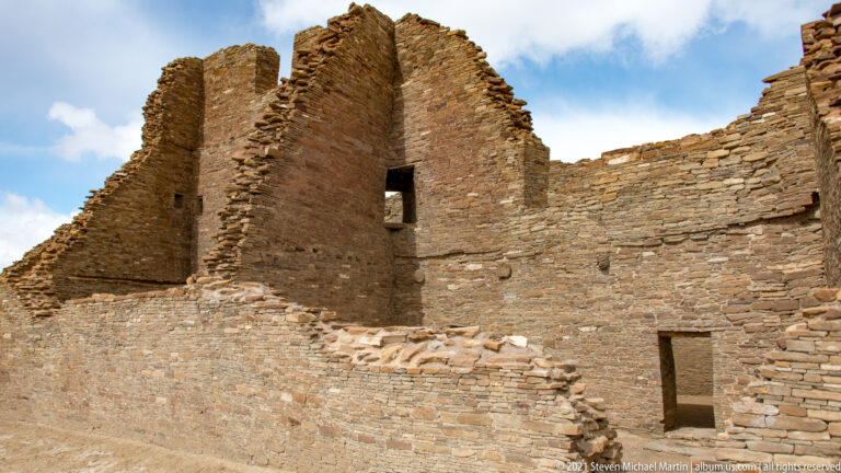 High stone walls with an upper window and lower doorway rise above a connected room block.