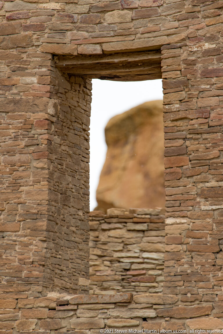 A rectangular stone window frames a distant sandstone butte above a low masonry wall.