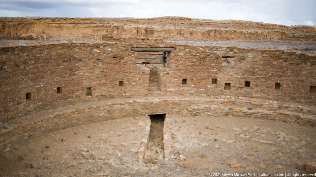 A circular masonry chamber has evenly spaced wall openings and a narrow passage leading toward a central doorway.