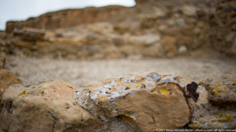 Yellow and gray lichen covers the rough top of a sandstone wall in a close detail.