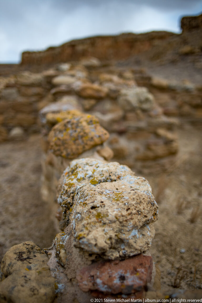 A pale lichen-covered stone rests on a darker slab, with blurred masonry behind it.