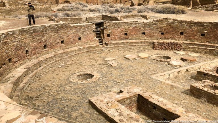 An excavated circular stone enclosure contains smaller circular and rectangular features within its walls.