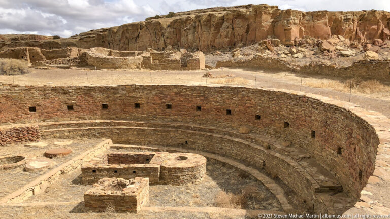 A curved masonry wall encloses rectangular and rounded features inside a sunken archaeological structure.