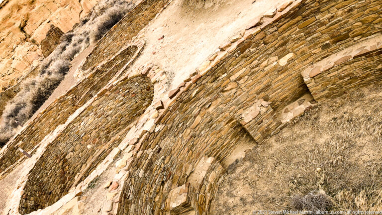 Thin stone courses curve diagonally across the frame, with larger blocks and a small square opening.