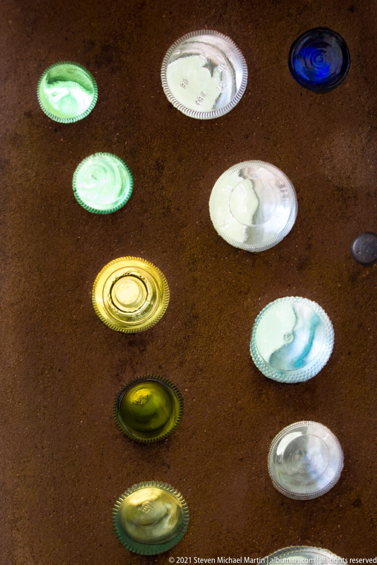 Colored bottle bases are embedded in a brown wall, forming scattered circular accents.