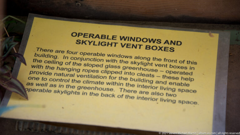 A yellow sign describes operable windows and skylight vents for natural ventilation in a greenhouse ceiling.