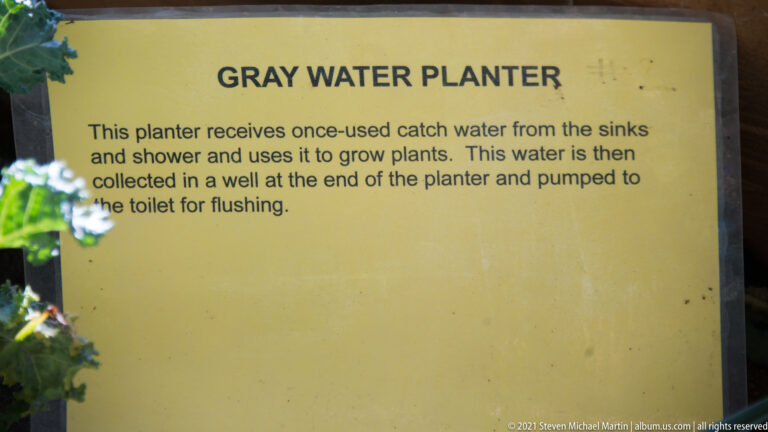 A Gray Water Planter sign explains that sink and shower water nourishes plants before being reused to flush a toilet.