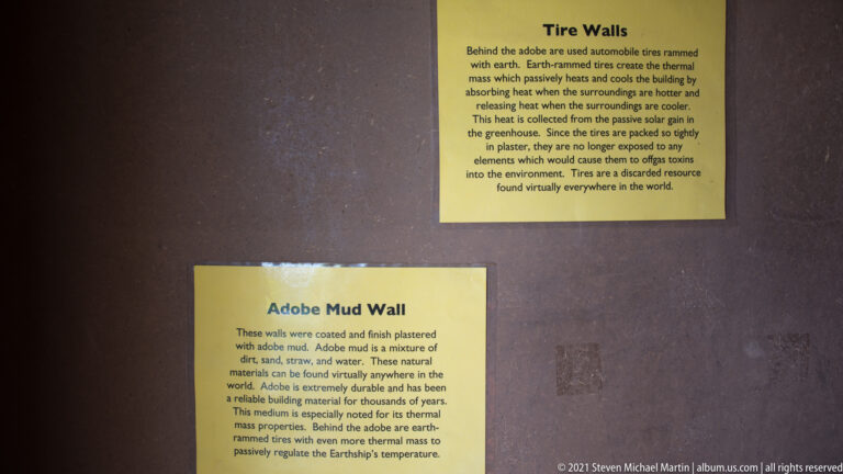 Paired signs explain earth-packed tire walls and adobe mud walls against a dark display surface.