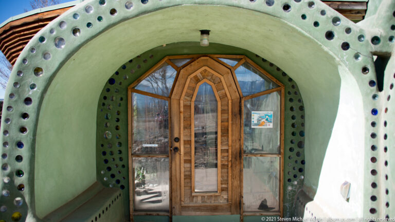 A wood-and-glass door sits inside a rounded pale green entry wall dotted with circular glass openings.