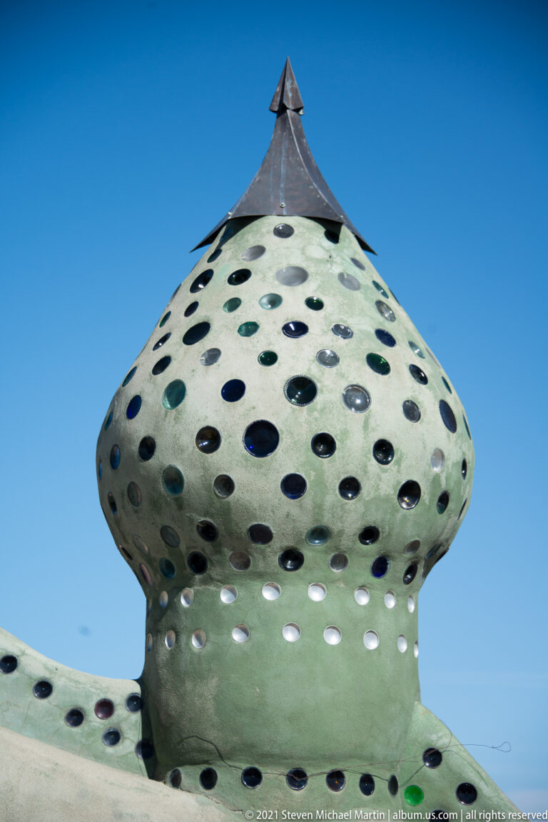 A rounded green roof projection with many circular glass openings rises against a clear blue sky.