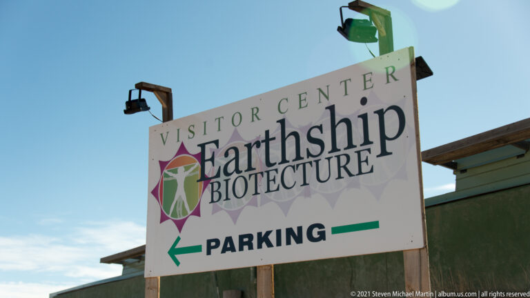 A roadside sign for the Earthship Biotecture Visitor Center points left toward parking.