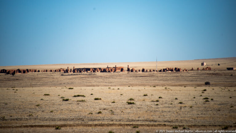 Low adobe ruins with broken walls and chimneys stretch across an open prairie.