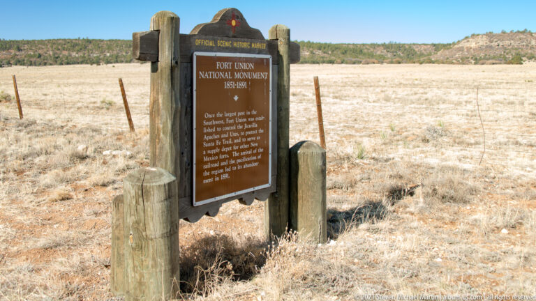 A brown Fort Union National Monument historic marker stands between wooden posts in grassland.