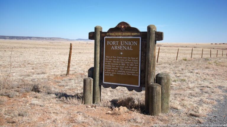 A brown Fort Union Arsenal sign hangs between timber posts in open grassland.