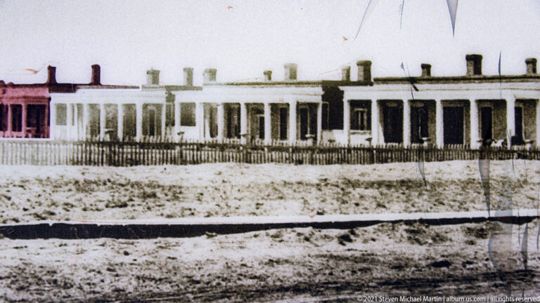 Archival black-and-white photograph shows a long barracks building with a repeated row of windows.