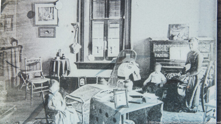Black-and-white interior photograph shows several people among tables and chairs near a large window.