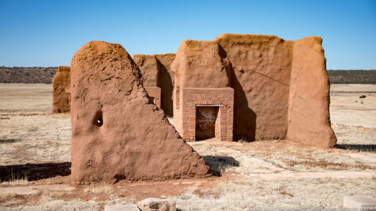 Dark doorway with brick edges opens through a weathered adobe wall in close view.