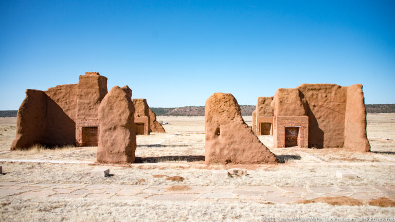 Two brick-framed doorways appear in separate adobe wall sections divided by lower ruins.