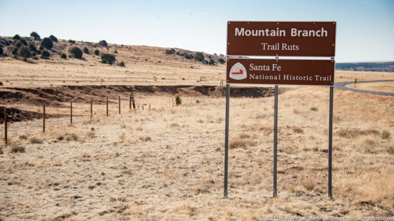 A brown sign identifies Mountain Branch Trail Ruts on the Santa Fe National Historic Trail beside open grassland.