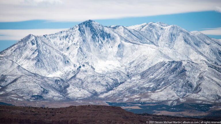 A snow-covered mountain range rises beyond a red-brown desert rim.