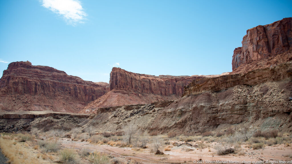 Red sandstone walls enclose a pale rocky wash with sparse shrubs.