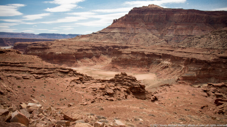 A pale river curves through a broad red-rock canyon below a flat-topped butte.