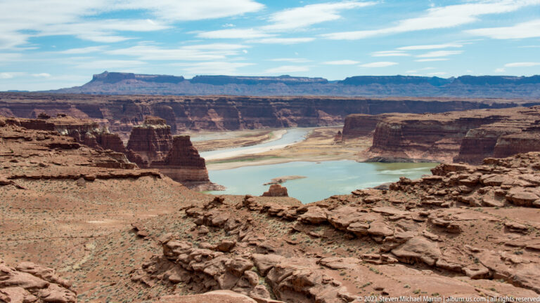 Blue-green water winds between layered red and brown canyon walls.