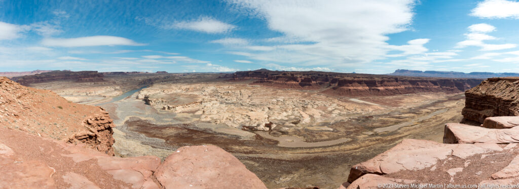 A dark river curves through a wide layered canyon seen from a high rocky overlook.