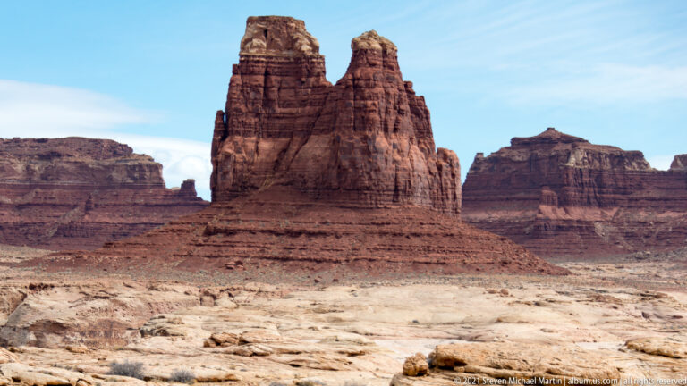 Two narrow sandstone towers rise above a pale plateau with dark mesas behind them.
