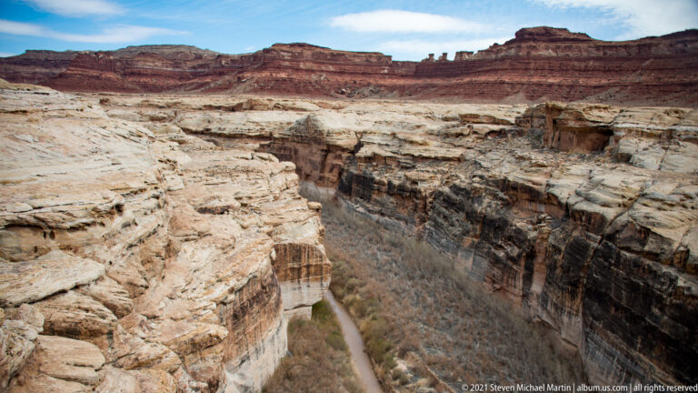 A narrow stream and leafless trees lie at the bottom of a deep, steep-walled canyon.