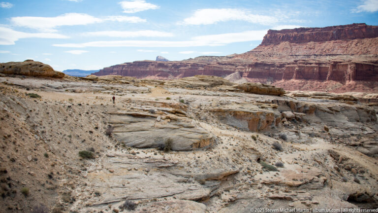 A lone visitor stands on pale slickrock before distant red canyon walls.