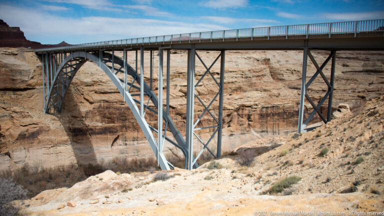 A steel arch bridge with lattice bracing spans a pale sandstone gorge.
