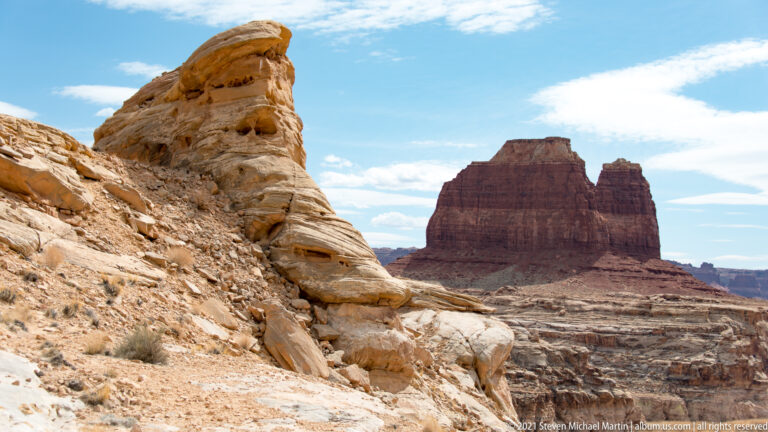 A pale sandstone outcrop in the foreground frames a dark flat-topped mesa across a layered canyon.