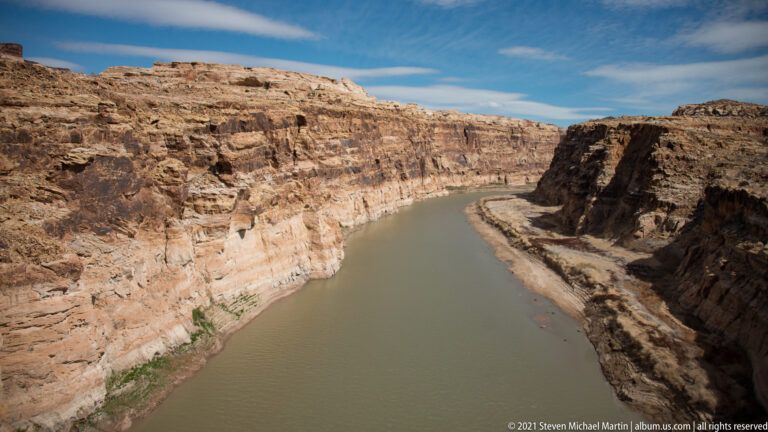 A muted green river curves between steep layered sandstone walls and pale rock shelves.