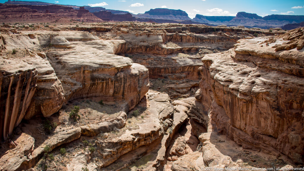 An expansive overlook shows pale sandstone shelves, deep canyon cuts, and mesas along the horizon.