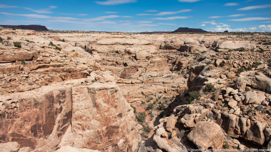 Pale sandstone shelves and gullies lead toward a dark mesa above a deep canyon cut.
