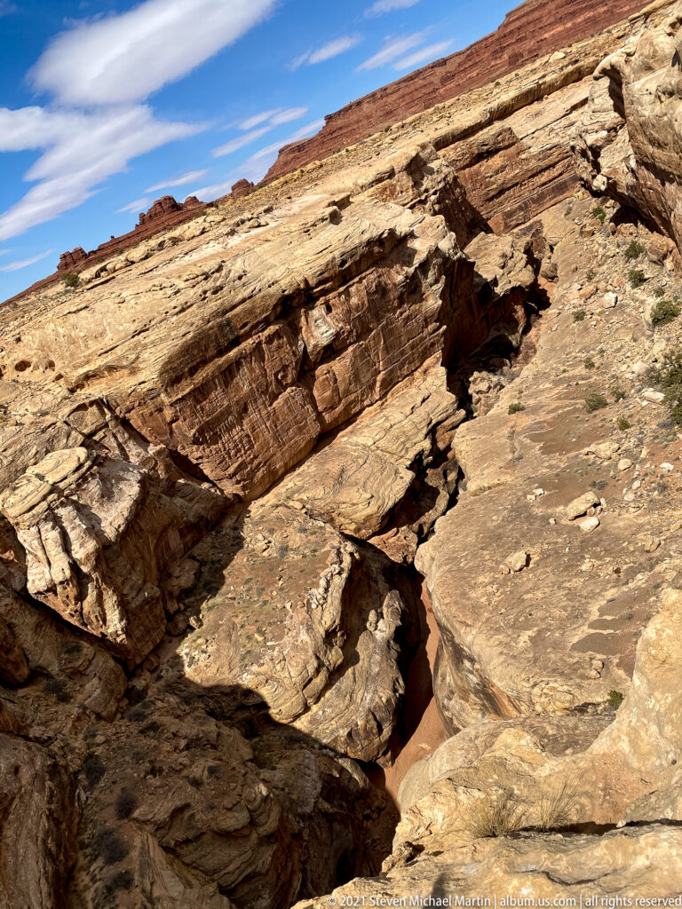 Angular sandstone layers and fractured slabs surround a deep shadowed crack.
