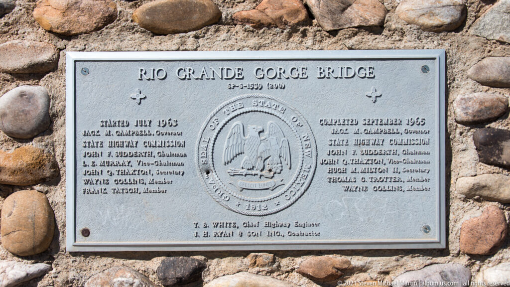 A metal Rio Grande Gorge Bridge plaque is set into a wall of rounded stones.